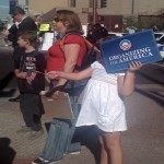 A young girl waves a sign supportive of Obama to protect herself from the sun and fan off the heat